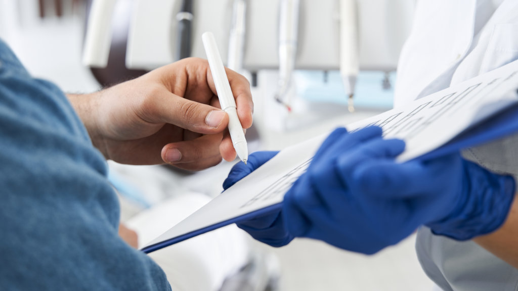 Patient filling out dental forms while dentist holds paperwork